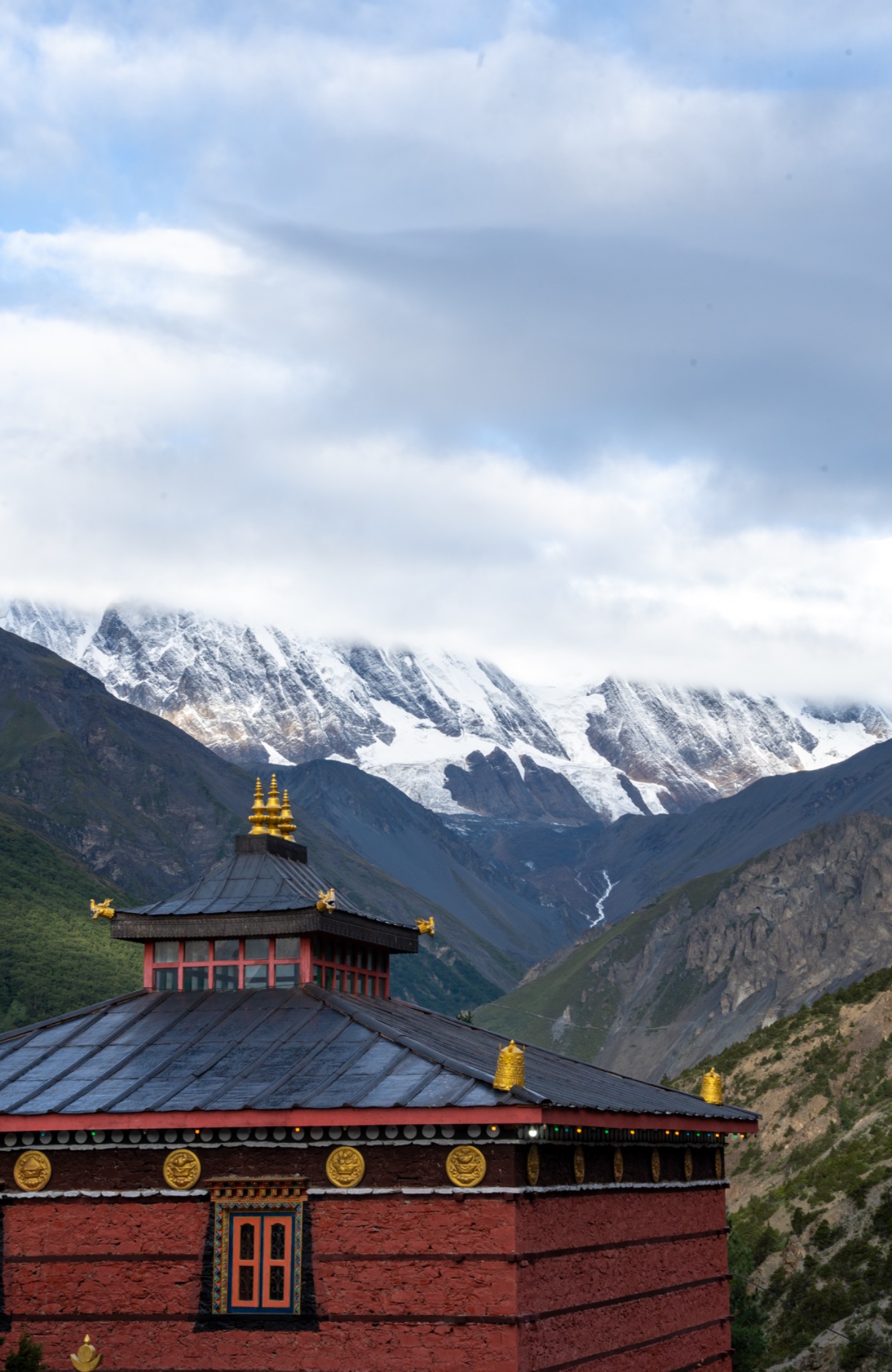 A red mountain monastery with snow-covered peaks behind it